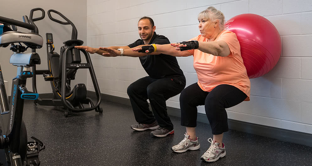 Physical therapist assistant does squats with a patient.